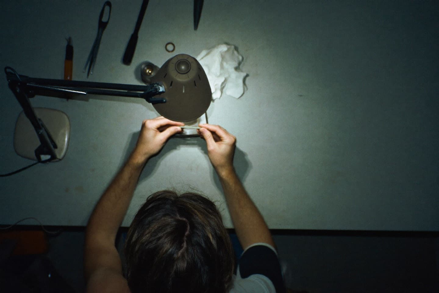 Hands working at a bench under a lamp